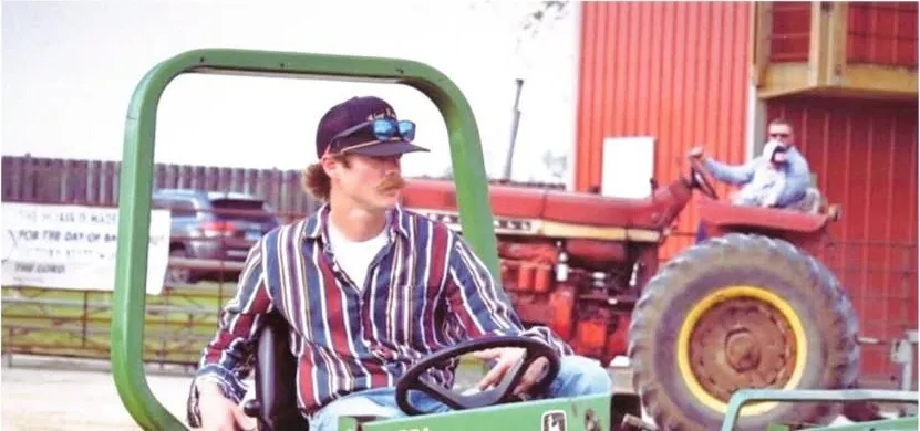 John Combs on a green John Deere tractor, in a cap and striped shirt